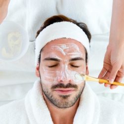 Portrait of man with clay facial mask in beauty spa.